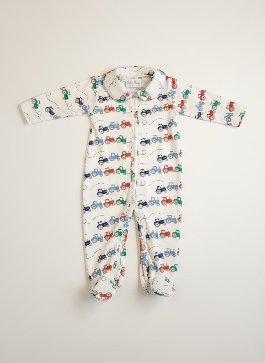 Rachel Riley for Bobbie's Shoppe white footed pajamas with all-over tractor print in red, blue, and green. Zipper closure.